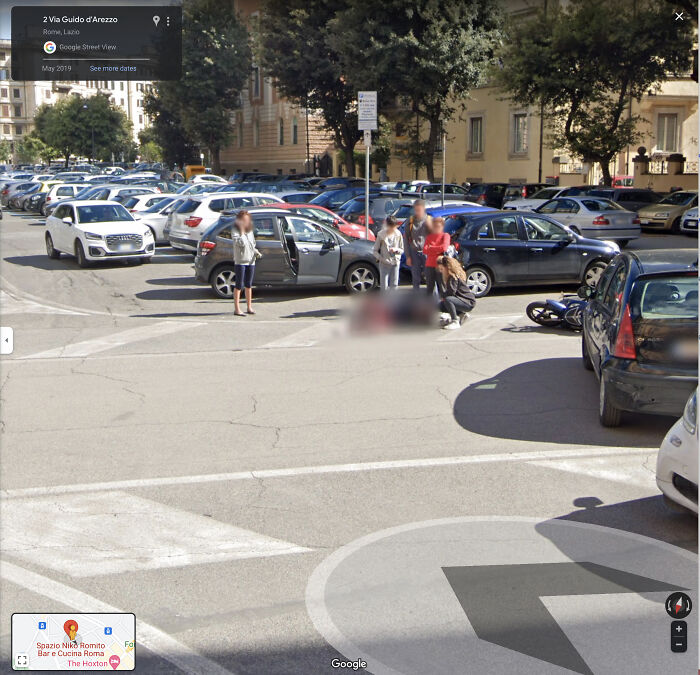 A busy street scene with cars, a crowd of people gathered around a blurred area on the ground, an odd Google Maps find.
