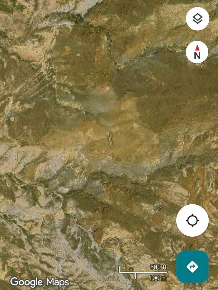 An aerial view from Google Maps showing a barren, rocky landscape with a small, green rectangular shape in the distance. The image is an odd find on Google Maps.
