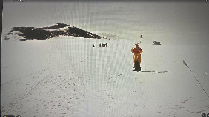 A person in a yellow suit stands in a vast, snow-covered landscape with mountains in the background. The image is an odd find on Google Maps.