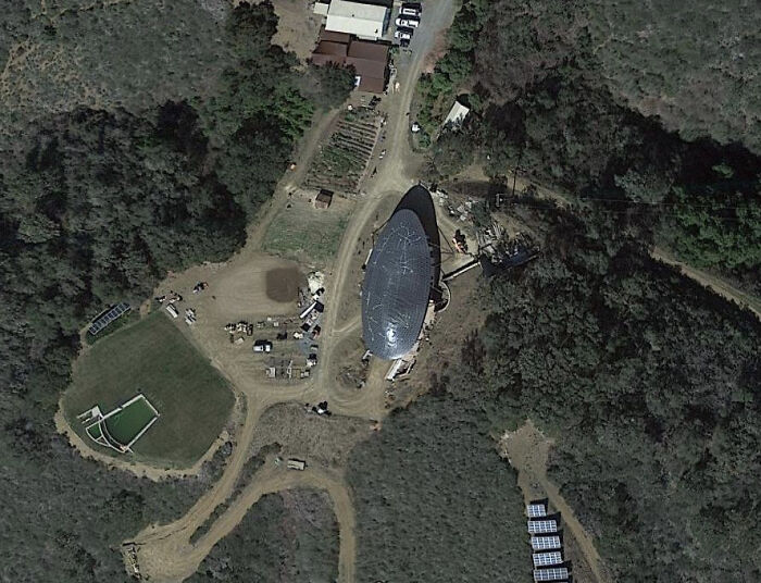 An aerial view from Google Maps showing a rural landscape with a large, dark, elongated structure. The image highlights an odd find on Google Maps.