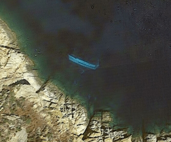 A shipwreck visible underwater near a coastline, an odd thing found on Google Maps.