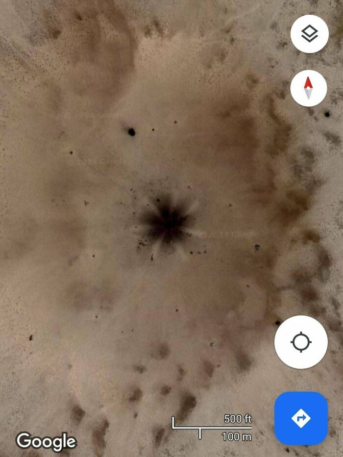 A Google Maps satellite image displaying a large, dark, starburst-like anomaly in a barren, sandy landscape, an odd find.
