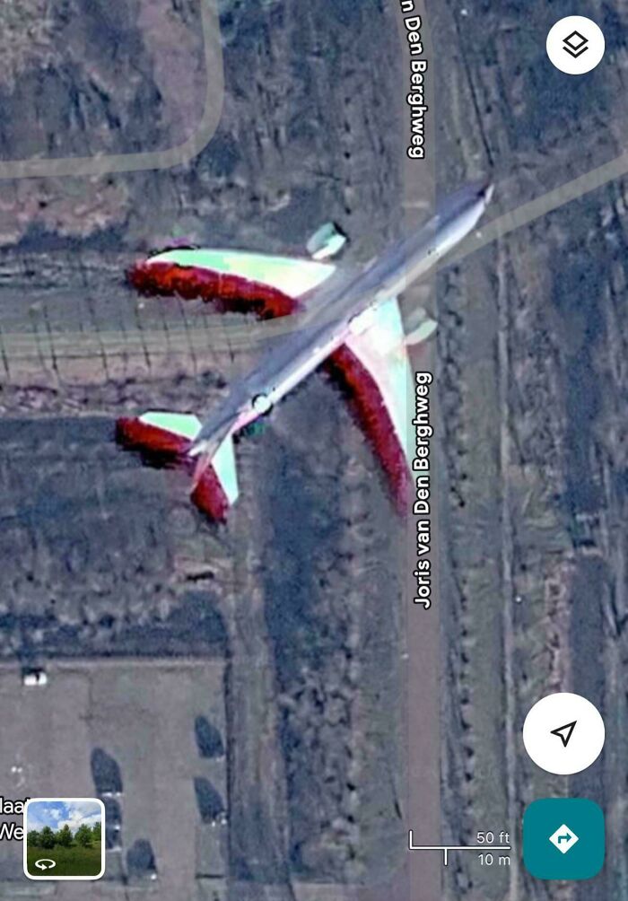 An airplane on the ground, captured on Google Maps, showing a red and white plane near a road.