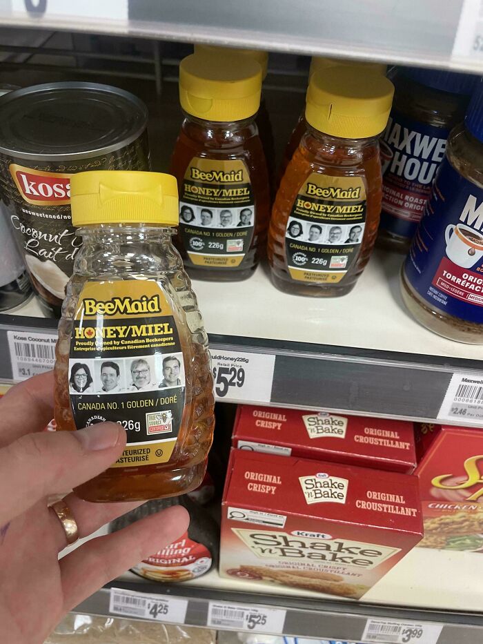 A hand holding a small bottle of BeeMaid honey, with more honey bottles and other groceries in the background. Little hope for humanity.