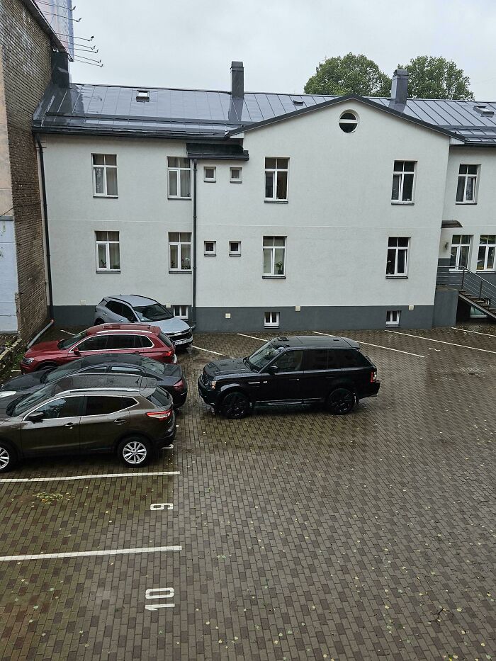 A black SUV parked incorrectly, taking up multiple spots, showing little hope for humanity in parking etiquette.