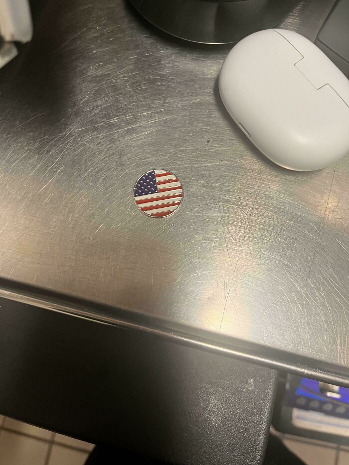 A small round American flag pin on a metal surface, illustrating a lack of hope for humanity.