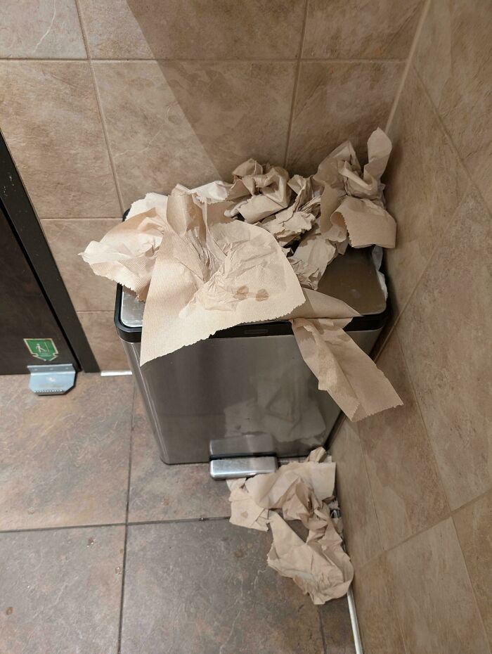 An overflowing trash can with paper towels on the floor, showing little hope for humanity.