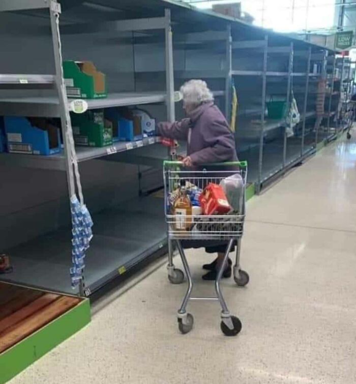 An elderly woman pushing a shopping cart through empty supermarket shelves, reflecting little hope for humanity.