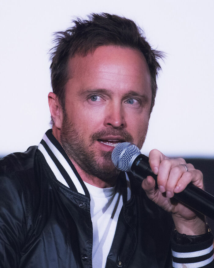 Aaron Paul speaking into a microphone, highlighting his bio and career.