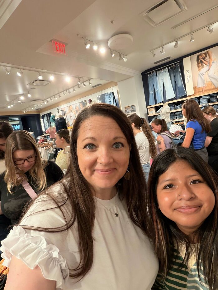 Two women smiling for a selfie in a busy retail store, a real deal moment of happiness.