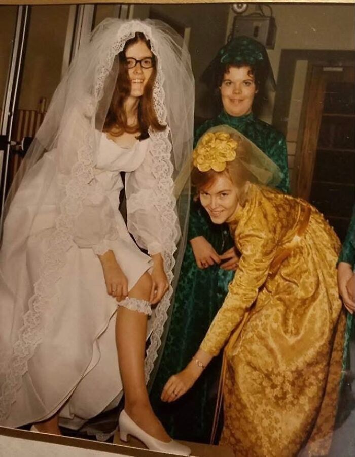 A vintage photo of a bride wearing glasses and a garter, with two bridesmaids in green and gold dresses, a sign of enduring love.