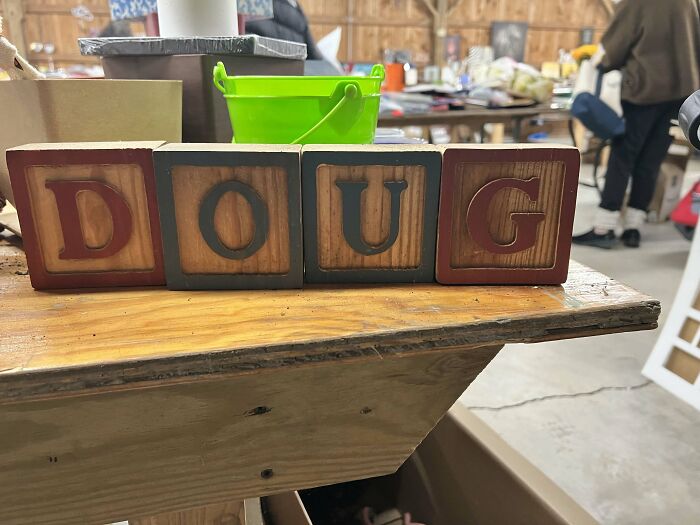 Four wooden blocks spelling out the name DOUG, sitting on a rustic wooden table amidst other items. A sign from the universe.