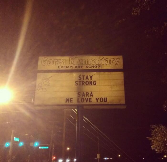 A warmly lit sign for Garza Elementary at night, displaying a message: Stay Strong Sara We Love You. A sign from the universe.