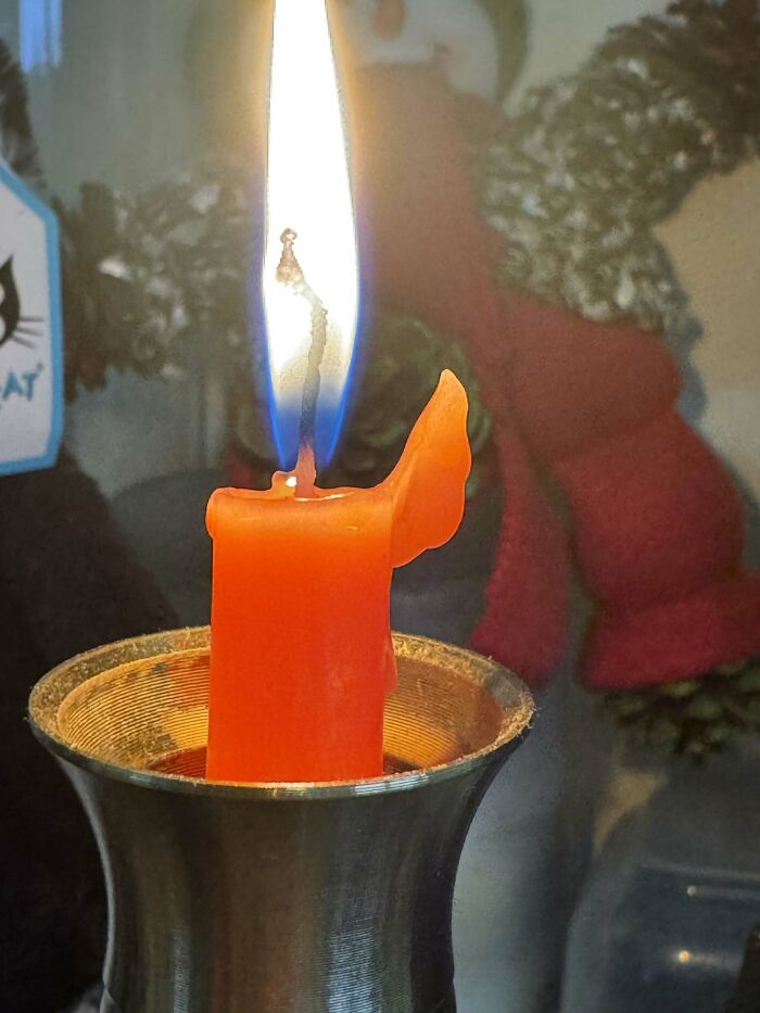 A lit orange candle with a bright flame, melting into a unique, wing-like shape. A sign from the universe.
