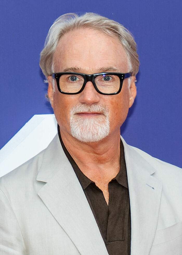 David Fincher, a renowned director, with gray hair, a goatee, and black glasses, in a light jacket. This image highlights David Fincher's distinctive look and career.