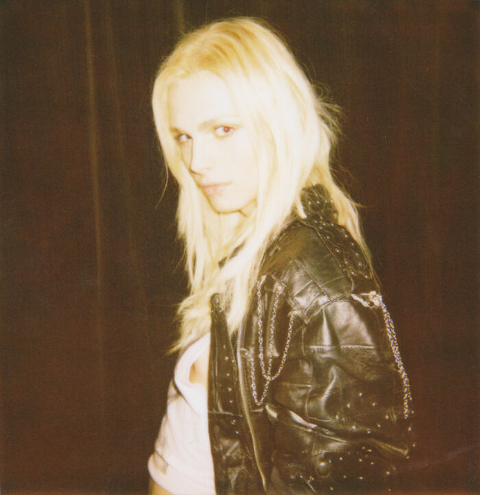 Andreja Pejić with long blonde hair, wearing a black leather jacket over a white top, looking directly at the camera.