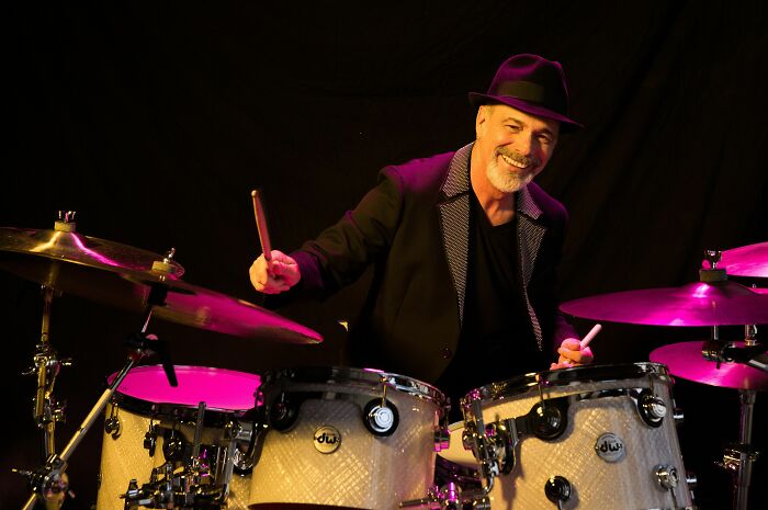 Danny Seraphine smiling while playing drums, highlighting his career in music.
