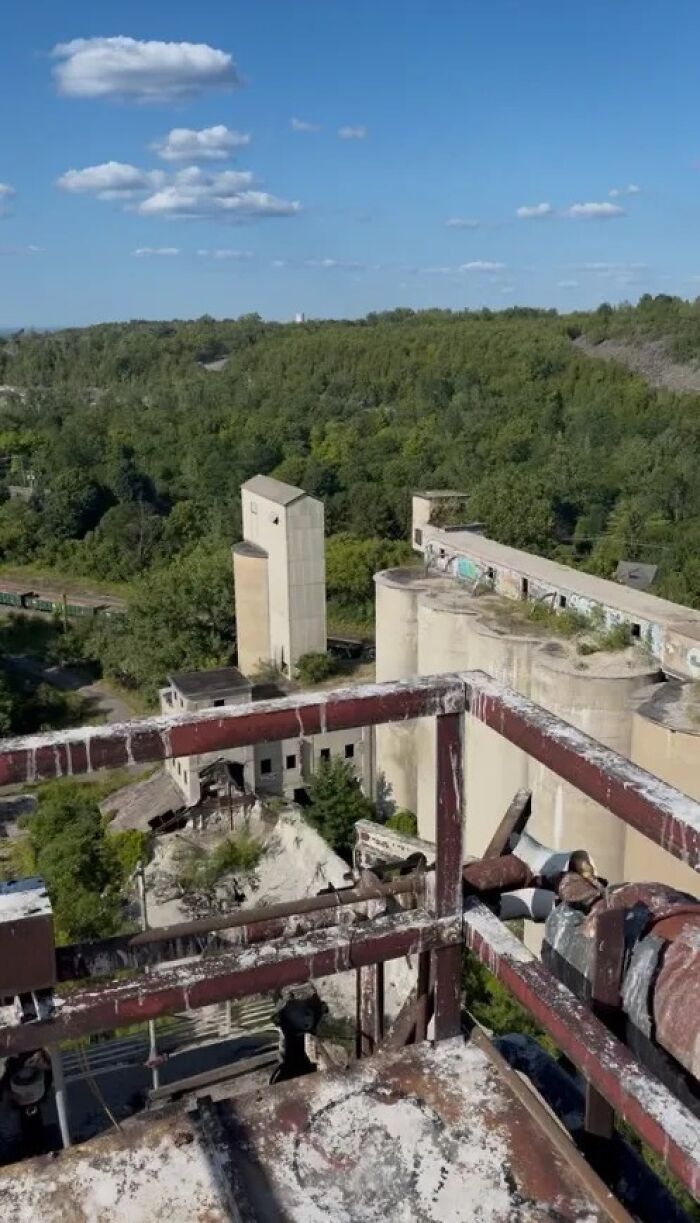A high-angle view of an abandoned industrial complex surrounded by lush green trees, perfect for urban exploration of forgotten places.