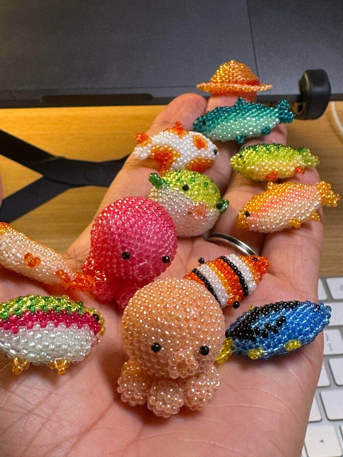 Amazing crafts: a hand holding many tiny, colorful beaded sea creatures, including fish, octopus, and crabs.