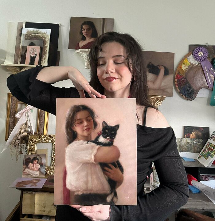 Amazing crafts: a young woman proudly displaying her oil painting of herself holding a black and white cat.