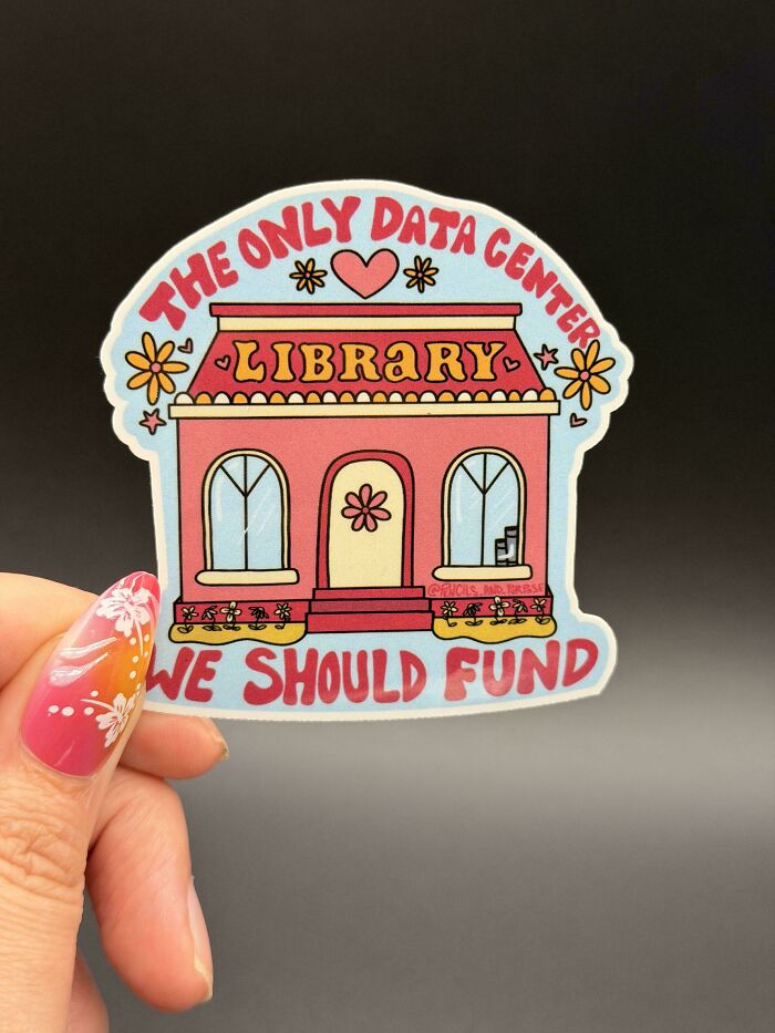 A hand holding a sticker of a pink library building with text The Only Data Center We Should Fund. Amazing crafts.