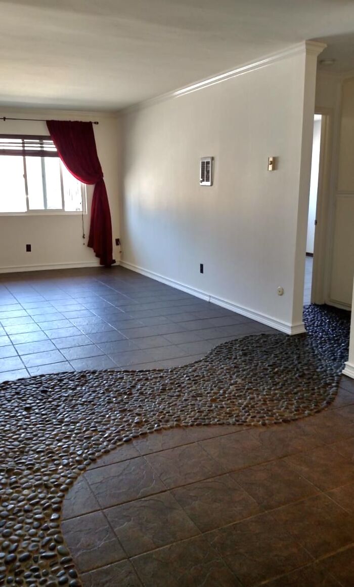 An indoor living space with dark tiled floors partially covered by a flowing river of polished stones, an awful idea executed with skill.