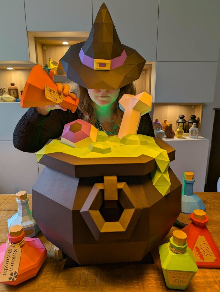 Woman in a witch hat holding a paper cauldron surrounded by colorful potion bottles, exemplifying amazing crafts.