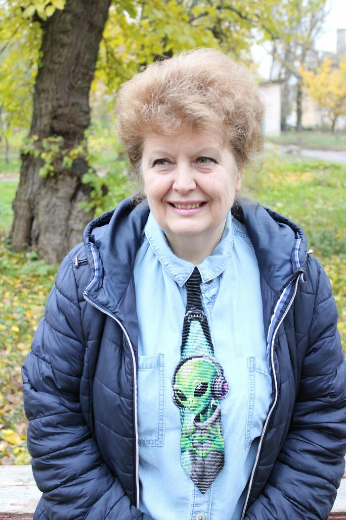 A smiling woman wearing a unique beaded tie featuring an alien in headphones, highlighting amazing crafts.