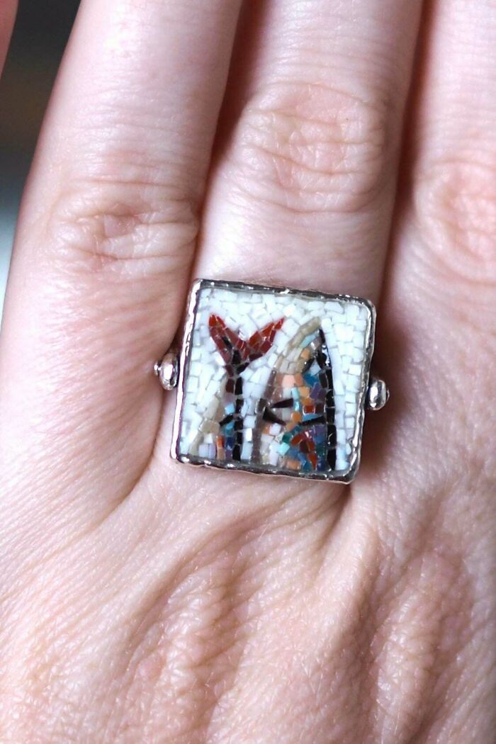 A close-up of a hand wearing a unique ring with a tiny, intricate mosaic design, an amazing crafts piece.