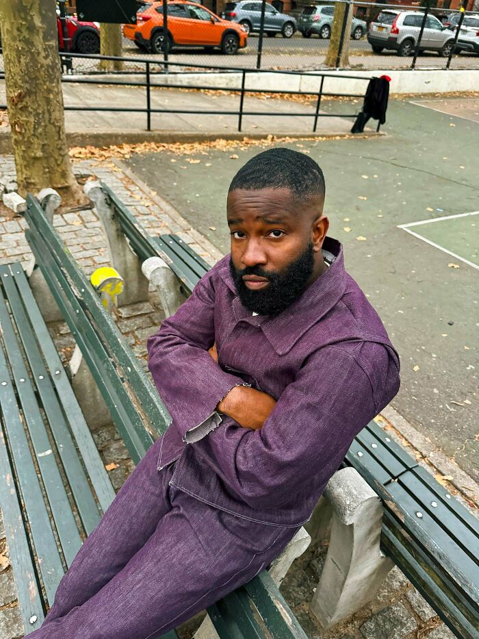 A man in a purple outfit sitting on a park bench, demonstrating amazing crafts in fashion.
