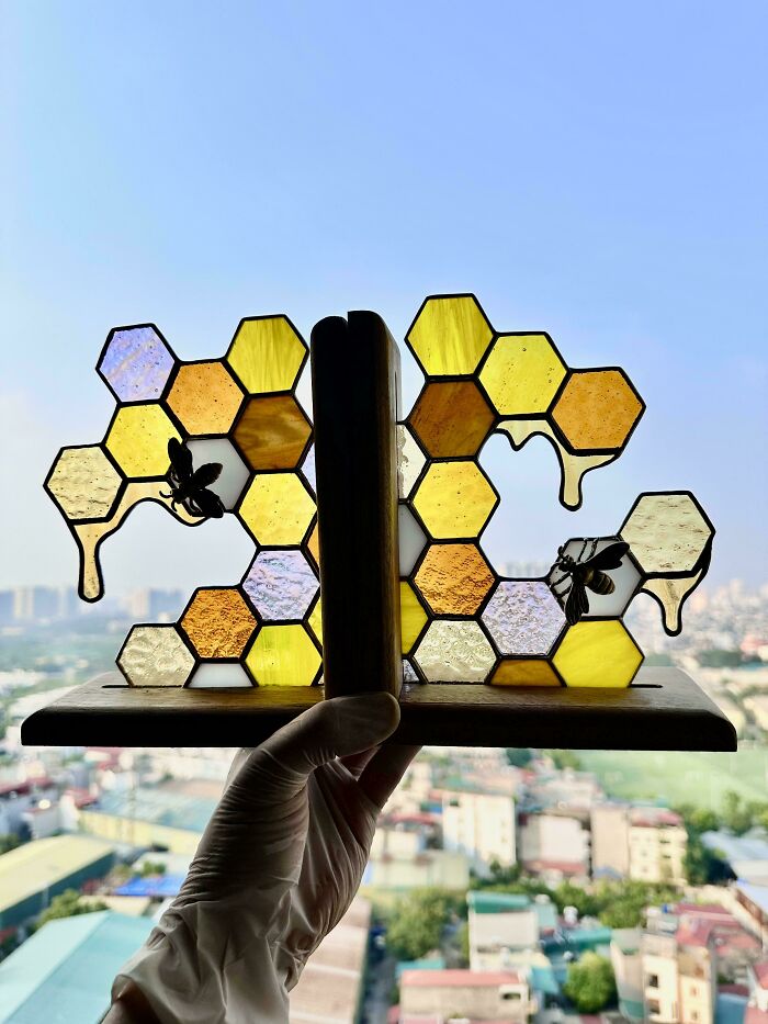 Amazing crafts: a hand holding stained glass honeycomb bookends with bees, set against a blurred city background, illustrating amazing crafts.