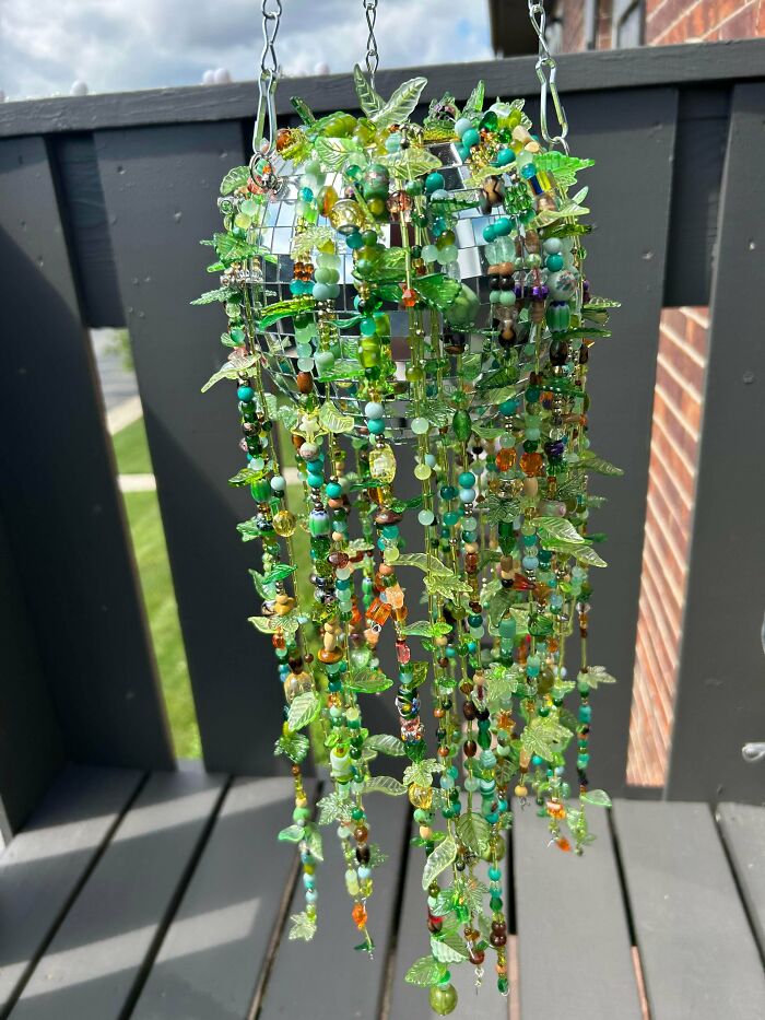 Amazing crafts: A hanging outdoor decoration made of green beads, leaves, and small trinkets on a sunny day.