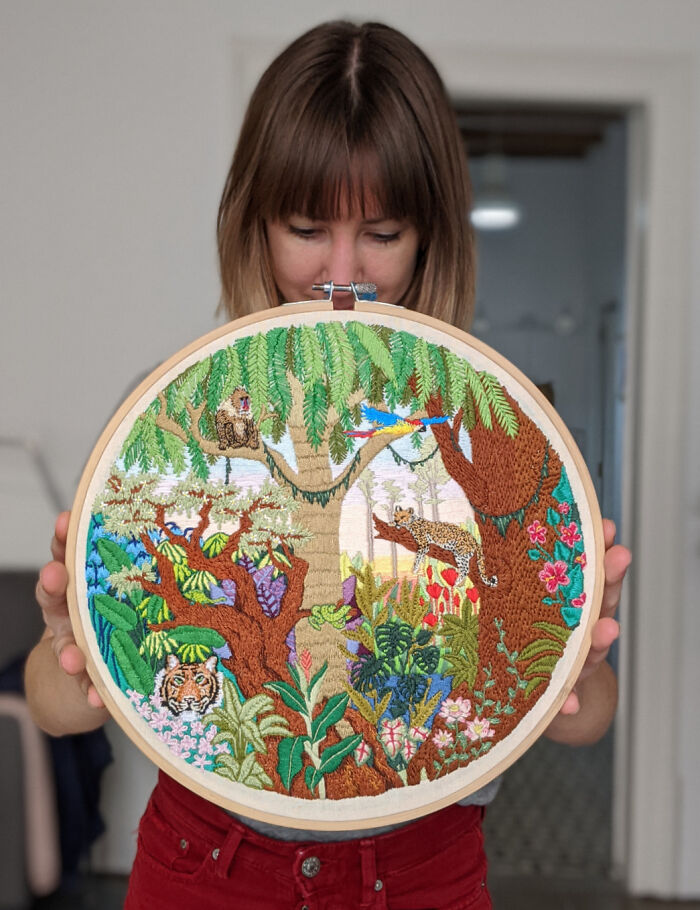 Amazing crafts: A person holding a beautiful, detailed embroidery hoop art depicting a vibrant jungle scene with animals.