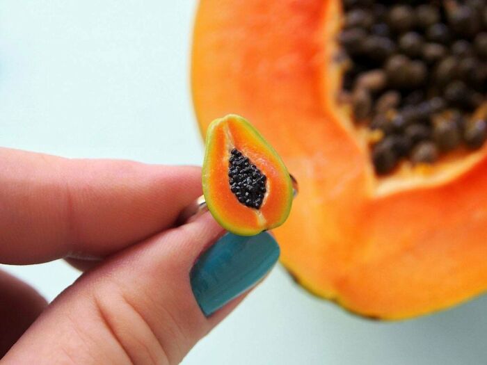 Amazing crafts: a miniature papaya ring held by a hand, with a real papaya in the background.