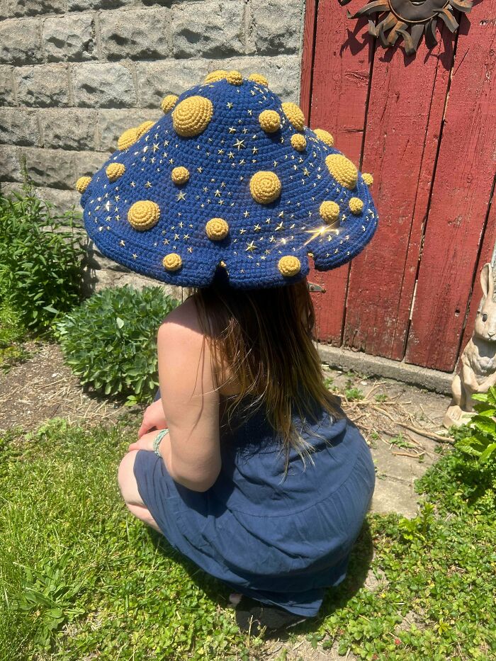 Amazing crafts: a person wearing an oversized, starry mushroom hat with yellow polka dots, demonstrating creative fashion.