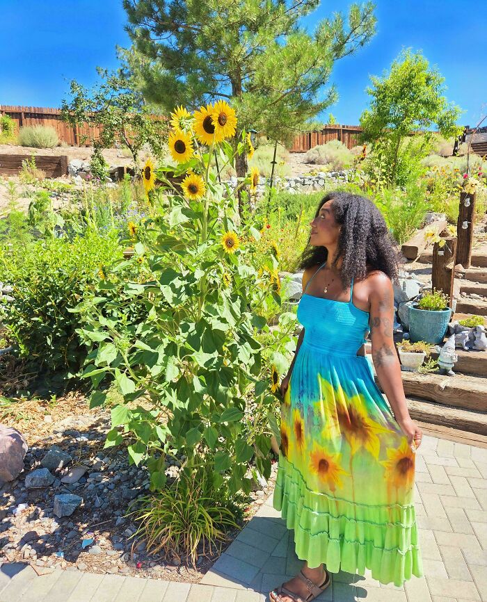 Amazing crafts: A woman in a sunflower dress standing next to tall sunflowers, capturing the beauty of nature and fashion.