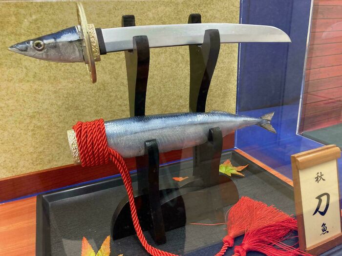 A fish-shaped sword and sheath displayed on a stand. An awful idea executed with disturbing skill.