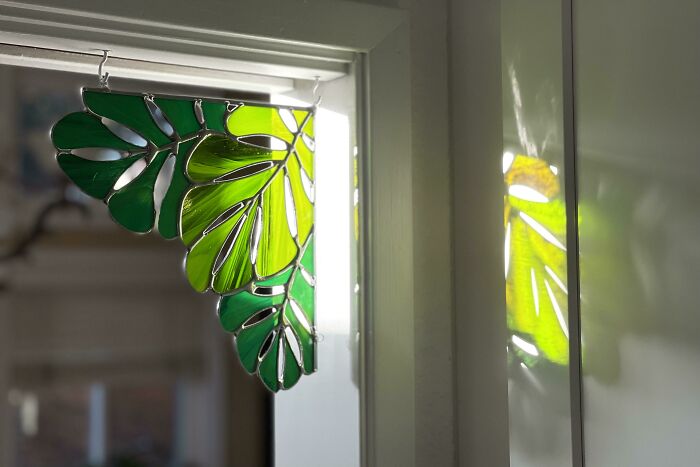 Amazing crafts: Stained glass art piece shaped like monstera leaves, hanging in a window, catching the light.