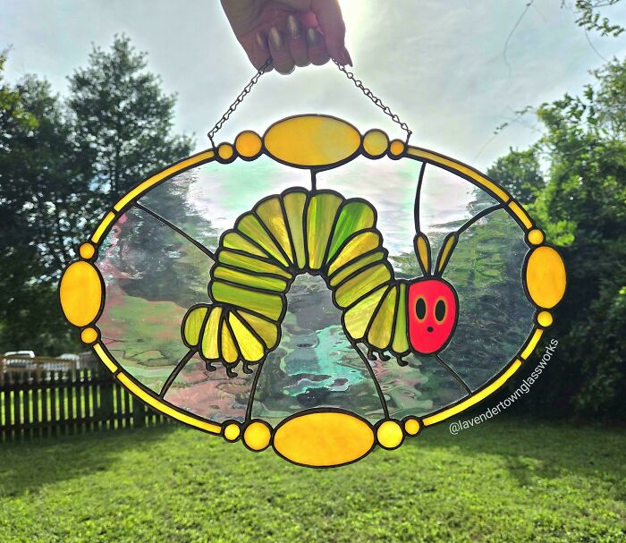 Amazing crafts: A vibrant stained glass art piece depicting a green caterpillar with a red head, held up against a sunny sky.