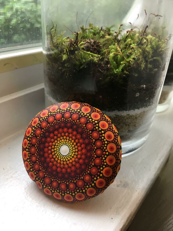 Amazing crafts: A beautifully hand-painted mandala rock with concentric circles of orange and red dots, next to a terrarium.