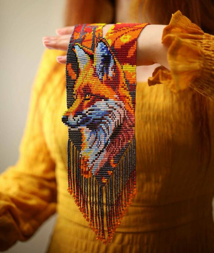 Amazing crafts: A person holding a detailed, colorful beaded necklace featuring a fox, demonstrating artistic talent.