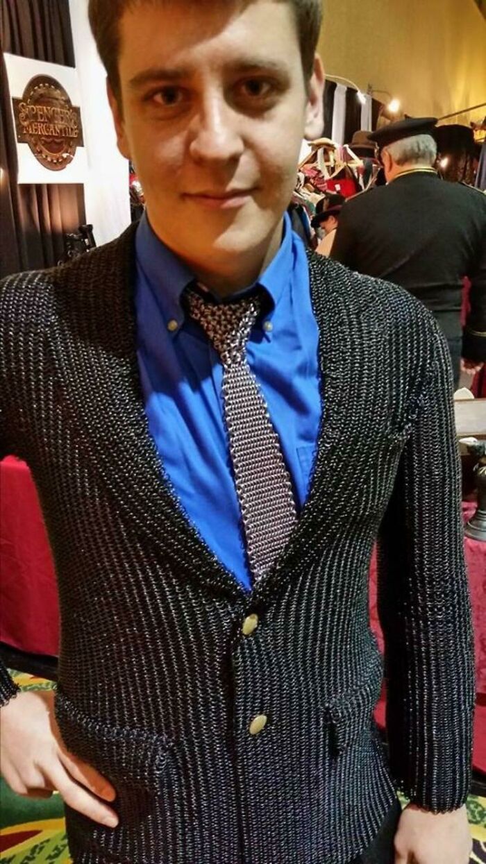A man wearing a chainmail suit jacket and tie over a blue shirt, an awful idea executed with skill.