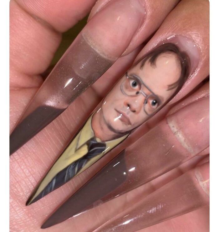 A close-up of a long acrylic nail featuring a detailed portrait of Dwight Schrute, an awful idea executed with skill.
