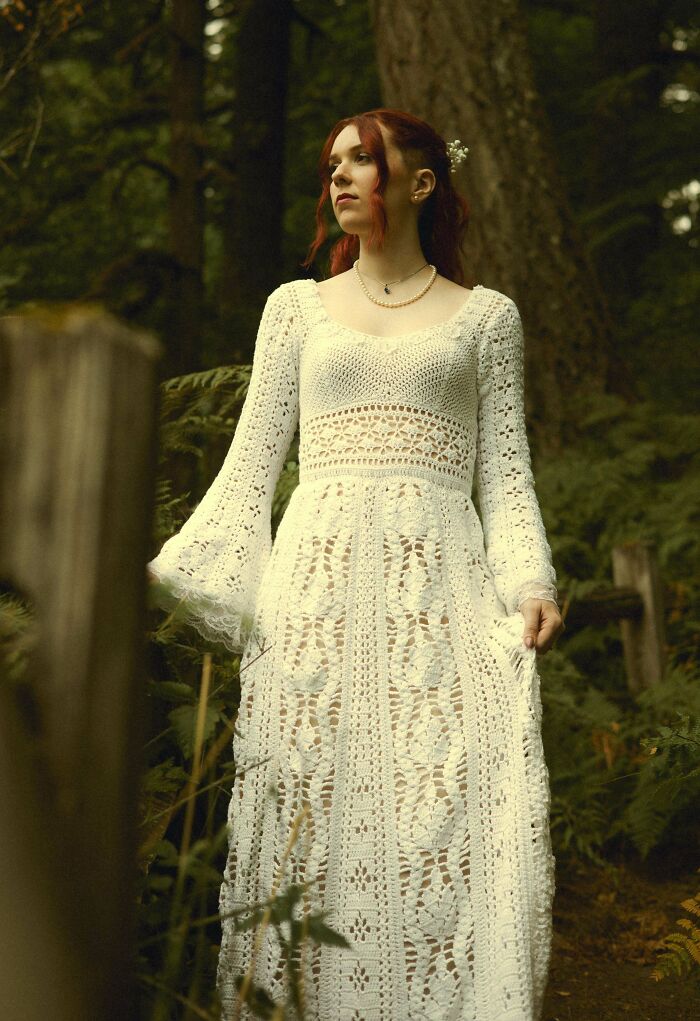 Woman wearing a white crochet dress standing in wooded area