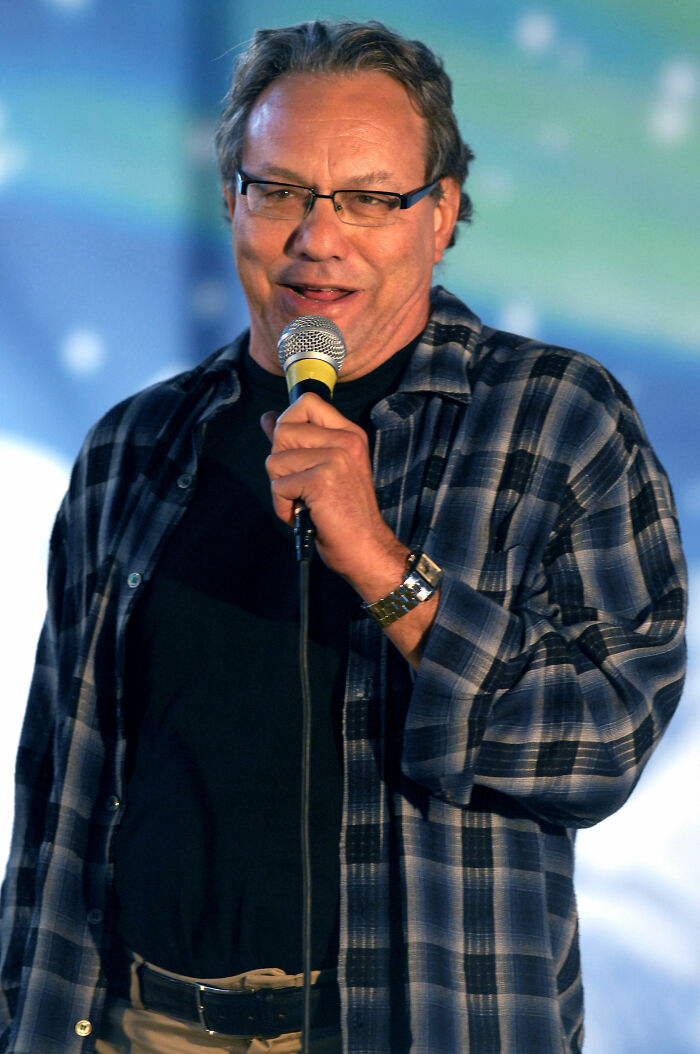 Lewis Black, a comedian, smiles while speaking into a microphone, showcasing his iconic career highlights.
