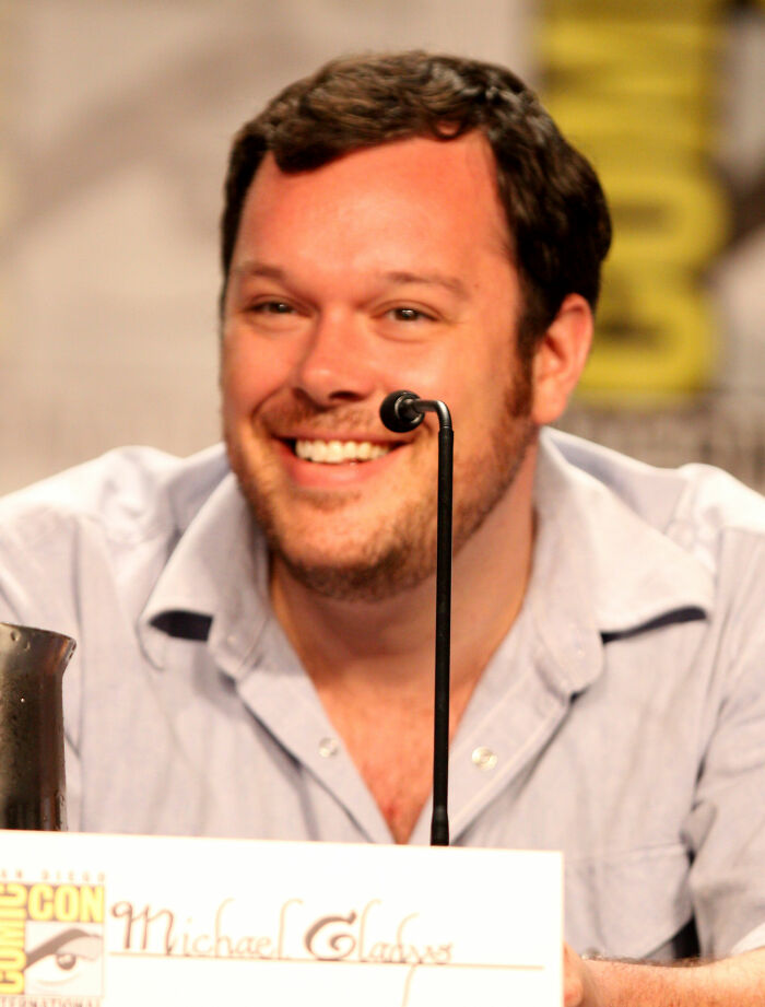 A smiling Michael Gladis speaking at an event, showcasing his career highlights and bio.