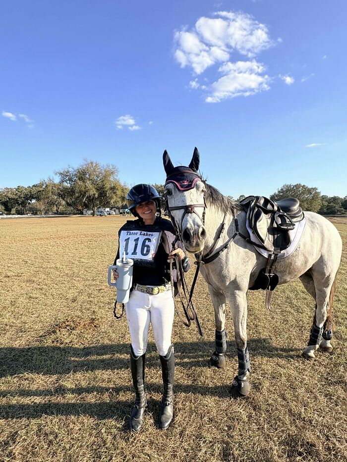 A rider stands next to a horse in a field, a beloved pet, which may incur vet bills for care.