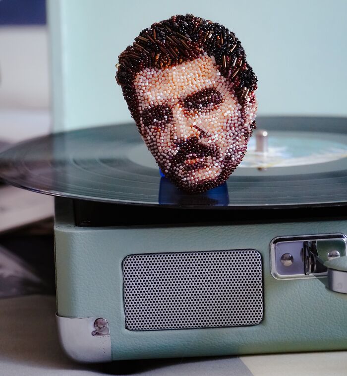 Beaded creation by Tiffany Pisani of Freddie Mercury's portrait brooch, meticulously crafted, placed on a vintage record player.
