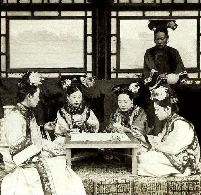 Four women in traditional attire playing a card game, an intimate moment lost to history.