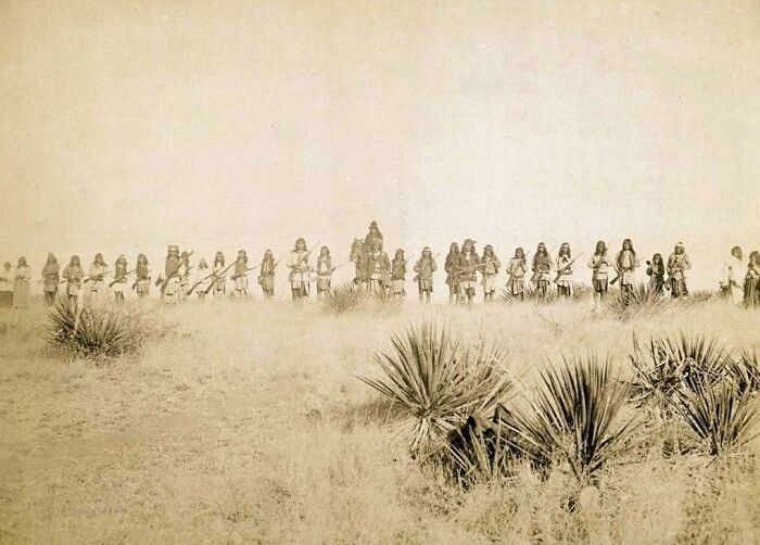 Historical photo showing Native American warriors in traditional attire across a vast, arid landscape, moments lost to history.
